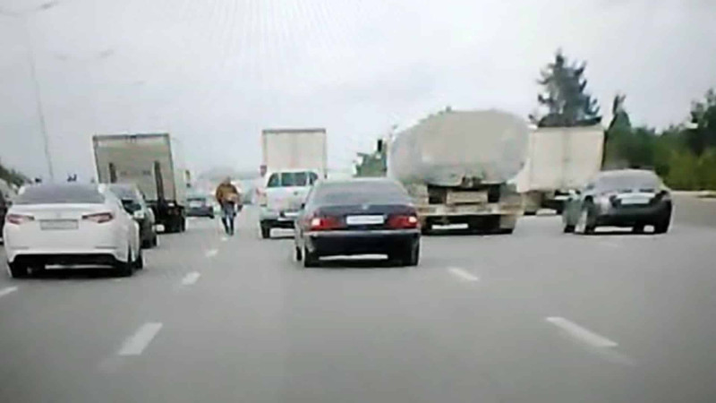 Piyada maşınların intensiv hərəkət etdiyi yol ilə gəzə-gəzə gedib